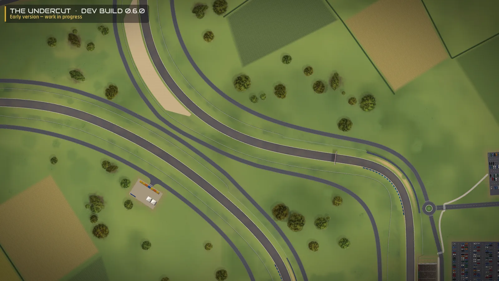 The Undercut 0.6.0 dev build — a closer view: the circuit with its gravel trap, an escape road, a service road leading to a roundabout and a car park, and fields beyond